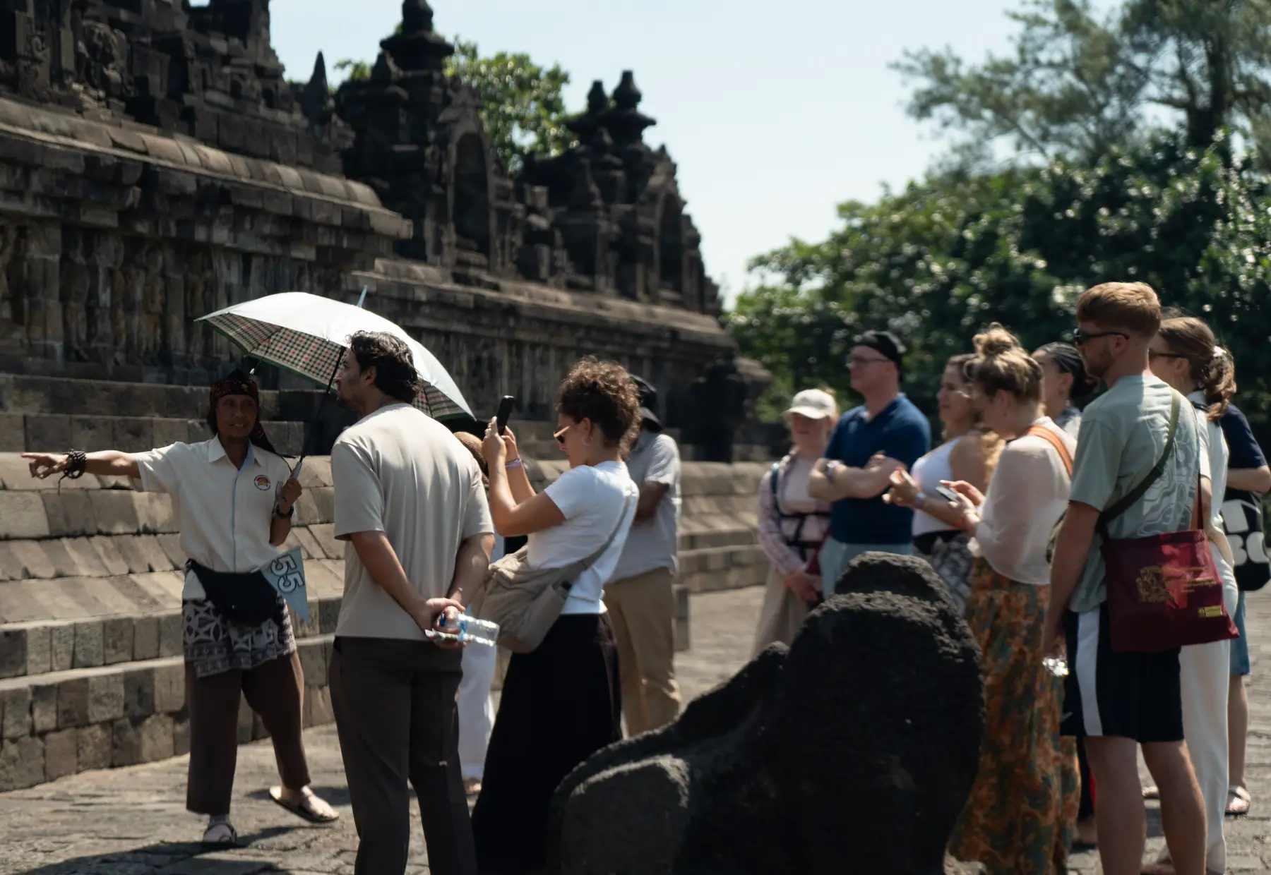 Tour guide briefing a group of visitors at an ancient stone temple in Indonesia